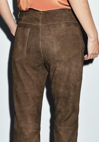 Brown suede pants with a soft texture, featuring two back pockets and contrasting stitching details, seen from the back view.