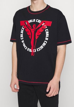 T-shirt noir à manches courtes avec des accents rouges et un grand imprimé graphique représentant une figure les bras étendus et un texte stylisé.