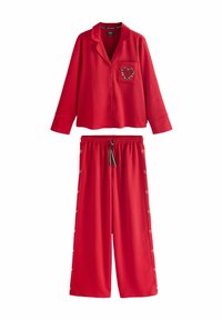 Punainen pyjama-asusetti, jossa on kauluksellinen nappitoppi, jossa on sydämen muotoinen tasku, sekä leveät housut, joissa on napit sivuilla. Pehmeä kangastuntuma.