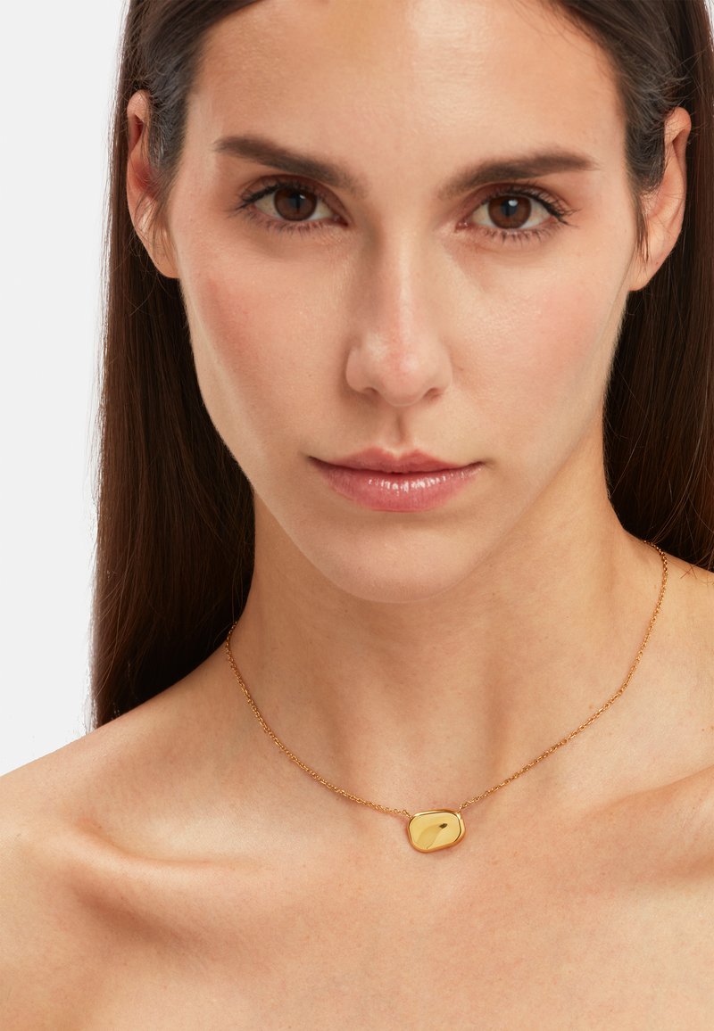 Collier en or avec un pendentif lisse et irrégulier sur une chaîne délicate, présentant une surface polie et de subtils reflets.