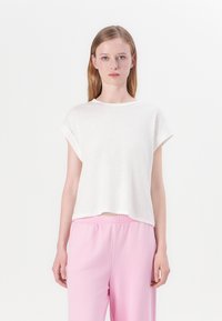 Hvid t-shirt med korte ærmer i en afslappet pasform med rund halsudskæring. Det lette stof har en subtil tekstur. Båret sammen med lyserøde sweatpants.