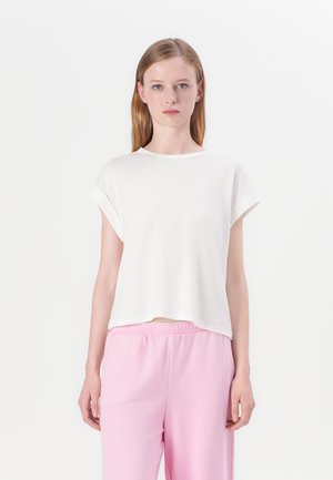 Hvit kortermet T-skjorte i en avslappet passform med rund hals. Det lette stoffet har en subtil tekstur. Kombinert med rosa joggebukser.