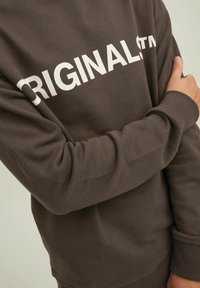 Brown sweatshirt with white "ORIGINAL" text. Features a crew neck, long sleeves, ribbed cuffs, and soft, textured fabric.