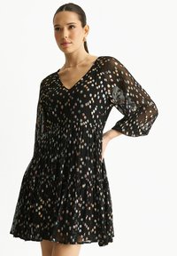 Black dress made of lightweight fabric featuring a V-neck, three-quarter sleeves, and a pleated skirt with multicolored dot patterns.