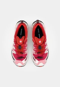Scarpe da corsa Salomon con tomaia in mesh rossa, rosa e bianca, suole in gomma nera e sistema di allacciatura elastico per una facile regolazione.