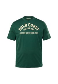 Zelené bavlněné tričko s kulatým výstřihem a krátkými rukávy; obsahuje bílý text: "GOLD COAST QUEENSLAND CHASING WAVES SINCE 2007."