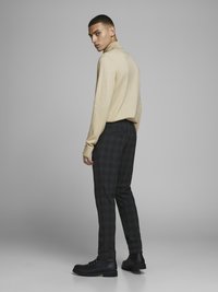Pull en tricot beige avec un col montant, associé à un pantalon à carreaux foncés et des bottes noires à lacets. Texture lisse, design ajusté et motif subtil.