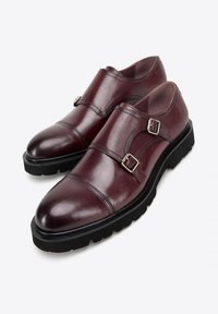 Burgundské kožené boty se dvěma přezkami, zaoblenou špičkou a kontrastní černou gumovou podrážkou. Hladký povrch a elegantní design.