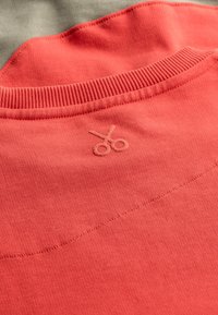 Rode katoenen sweatshirt met een geribbelde halslijn en een opgenaaid schaarlogo in lichtbruin. Gladde textuur met subtiele stikdetails.