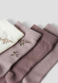Tre par strikkede sokker: én hvid med blomsterbroderi og to nuancer af lys mauve, både tekstureret og ensfarvet.
