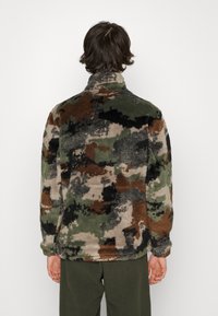 Fleecejakke med et camouflage mønster i grøn, brun og sort. Høj krave og elastiske manchetter, som giver en blød tekstur.