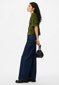 Top verde con paillettes e maniche corte abbinato a jeans di denim blu scuro a gamba larga. Borsa nera e scarpe con zeppa.