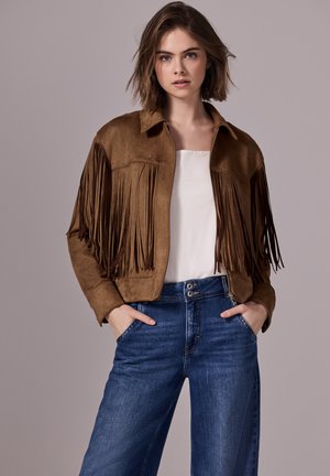 Brown suede jacket with fringe detail, collared and zippered front, paired with light blue wide-leg jeans. Simple white top underneath.