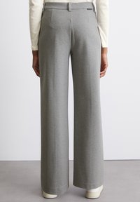 Un pantalon large gris avec une texture lisse et douce, doté d'une taille plate, de poches latérales et de détails minimalistes.