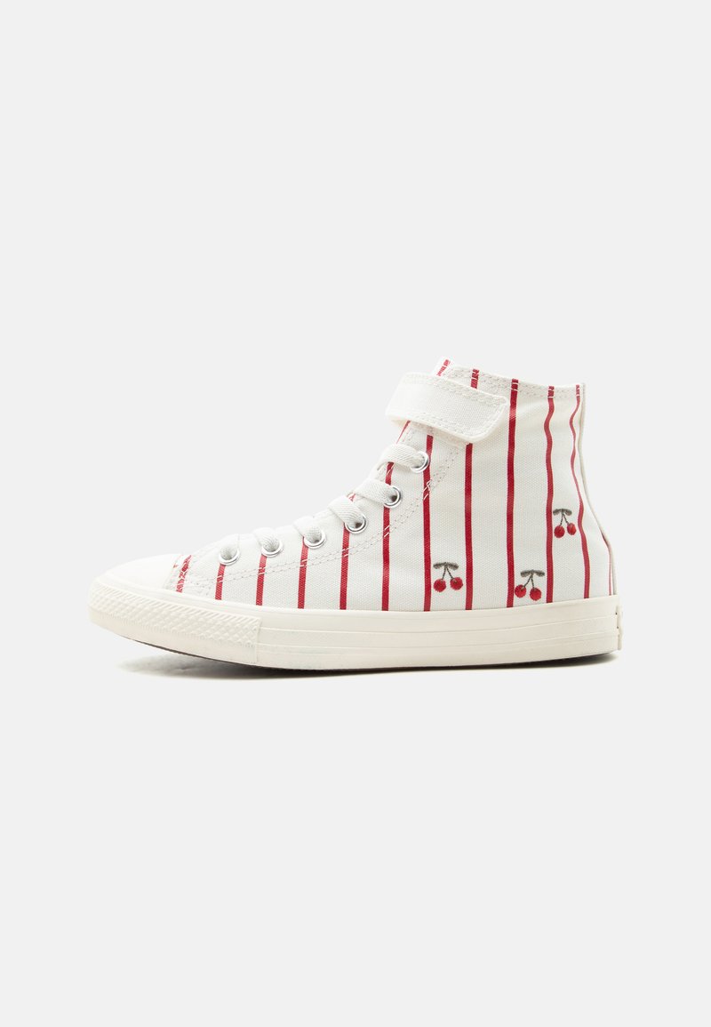 Baskets montantes blanches avec des rayures verticales rouges et petits motifs cerise, avec lacets et une bride Velcro sur fond uni.