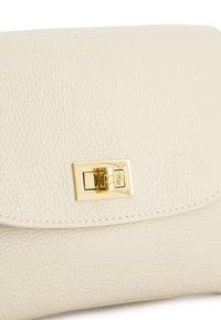 Cremefarbene Lederhandtasche mit Klappenverschluss und einem goldfarbenen Verschlussdetail, das sichtbare Nähte entlang der Kanten aufweist.