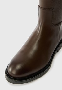 Brown leather ankle boot with a rounded toe, smooth texture, decorative stitching, and a black trim around the sole.