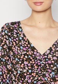 Vestido floral com fundo preto e pequenas flores em rosa, azul e branco, design de decote em V, feito de um tecido leve e suave.