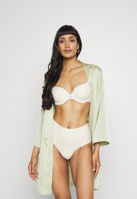 Accappatoio di raso verde chiaro sopra un reggiseno beige e una mutandina a vita alta. Texture liscia, colori solidi e design semplice senza motivi.