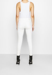 Jeans blancos ajustados con bolsillos traseros; tela suave y ligera; combinados con una blusa blanca sin mangas y botines negros de tacón alto.