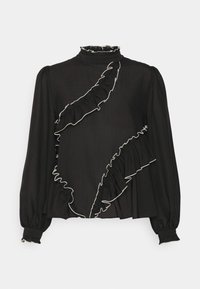 Svart blus med hög krage, med kontrasterande vit volangkant längs en diagonal söm och uppblåsta ärmar med strukturerade manschetter.