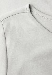 Tissu en coton gris clair avec une texture lisse, doté d'un col rond et de coutures contrastées. Vue en gros plan du matériau.