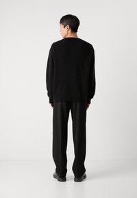 Black fuzzy sweater with long sleeves and ribbed hem, paired with black wide-leg trousers and black shoes, viewed from the back.