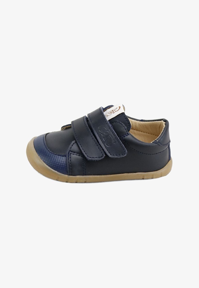Zapato para niño pequeño de color azul marino con dos correas de velcro, forro interior beige, puntera texturizada y suela de goma flexible marrón claro.