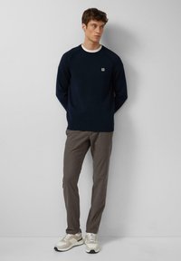 Granatowy sweter dzianinowy z raglanowymi rękawami, białym wykończeniem kołnierza i małym logo. W komplecie z beżowymi, teksturowanymi spodniami oraz beżowymi sneakersami.
