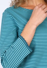 Langarmoberteil in teal und marineblauen Streifen, mit einem gewellten Saum an den Ärmeln und weichem, strukturiertem Stoff.