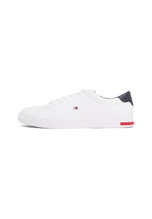 Baskets basses blanches avec languette de talon bleu marine, petit logo rouge et bleu sur le côté, lacets blancs et une bande rouge sur la semelle près du talon.