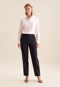 Camicia bianca a maniche lunghe con una texture morbida, abbinata a pantaloni sartoriali blu scuro con pieghe frontali e design a gamba dritta.