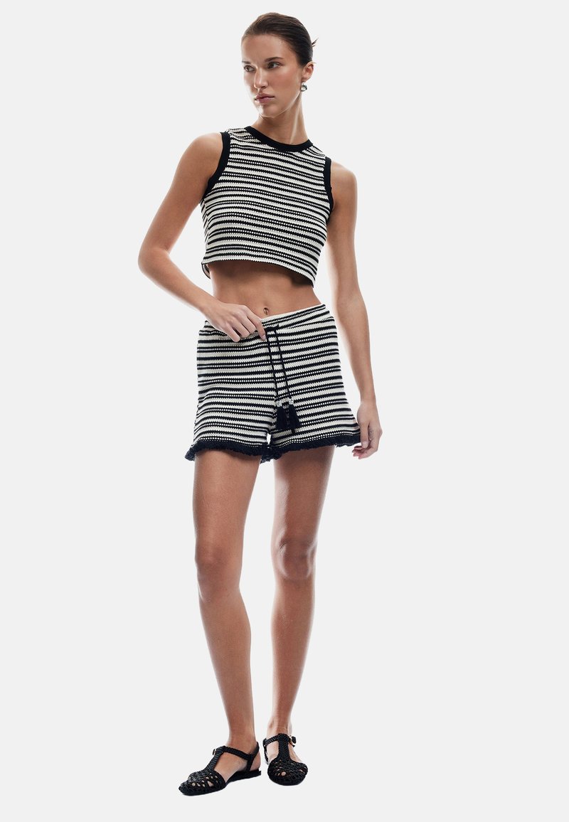 Conjunto de top corto de punto a rayas en blanco y negro y pantalones cortos con cintura ajustable y un adorno de borlas. Llevado con sandalias negras.