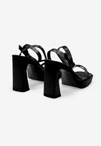 Sandalias negras de tacón alto con un tacón grueso, que cuentan con múltiples correas delgadas y un acabado suave. El tacón tiene una forma cuadrada.