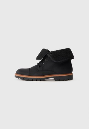 Botas de cuero negro con un collar de pelo negro deshilachado, que presentan cordones redondos, un acabado texturizado y una suela de goma con un patrón de tread definido.