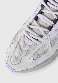 Close-up of light grey and lavender athletic shoe with mesh, suede, and synthetic overlays, white laces, and textured sole edge.