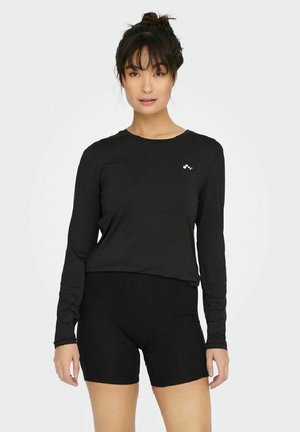 Top negro de manga larga con cuello redondo y un pequeño logo, combinado con shorts negros. La tela parece suave y ajustada.