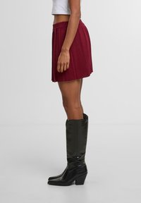 Burgundská skládací sukně s vysokým pasem, doplněná o vysoké černé lesklé boty s čtveratou špičkou a robustním podpatkem.