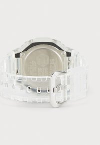 Montre transparente avec un bracelet en silicone, dotée d'un dos métallique argenté, d'un cadran rectangulaire et d'une boucle claire et ajustable.