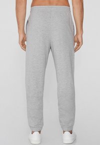 Gray sweatpants made of soft fabric with an elastic waistband, tapered legs, and side pockets. White sneakers complement the outfit.