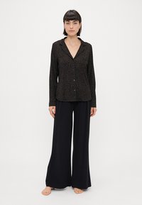 Camisa de manga longa com padrão de leopardo preto, com colarinho notched, frente com botões, combinada com calças largas pretas. Textura de tecido suave.