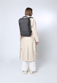 Schwarzer, rechteckiger Rucksack mit zwei Griffen und verstellbaren Trägern. Glatte, matte Textur; verfügt über zwei runde Akzente auf der Rückseite.