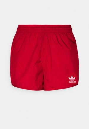 Czerwone spodenki sportowe Adidas z elastycznym paskiem w talii i białym logo koniczyny Adidas na dolnej prawej nogawce.