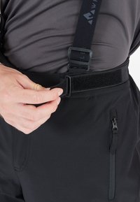 Zwarte broek met verstelbare banden en een klittenbandsluiting, voorzien van een ritszak en een strakke, gladde textuur.