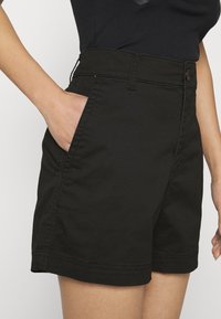 Černé bavlněné kraťasy s vysokým pasem, zapínáním na knoflíky, bočními kapsami a švy. Hladká struktura a přizpůsobený střih.