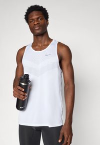 Men's Nike sleeveless tank top in white with textured pattern, round neckline, and side slits, held with a black water bottle.