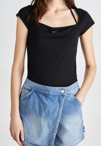 Svart kortärmad body med rundad halsringning, kombinerad med en ljusblå jeanskjol med asymmetrisk design och sidofickor.