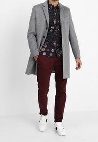 Harmaa villakangastakki, kukallinen musta paita, burgundi-housut, valkoiset tennarit mustilla yksityiskohdilla. Ominaisuuksiin kuuluvat napit, notche-lapeli ja teksturoitu kangas.