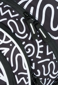 Zaino in tessuto nero con motivi astratti bianchi. Include zip nere con tiranti testurizzati e accenti bianchi lungo i bordi.