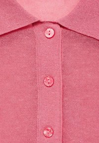 Polo shirt rosa lavorato a maglia con colletto e quattro bottoni trasparenti. Texture morbida con un delicato design a coste.